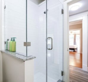 Un baño moderno con cabina de ducha de vidrio, encimera de granito y lavamanos a la vista.