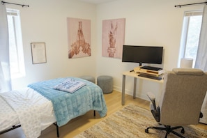 A bedroom with a bed, a desk with a computer, a chair, and two wall art pieces.