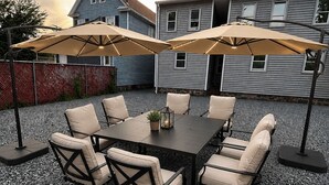 An outdoor patio with a table and chairs, surrounded by a gravel floor, under a cloudy sky. - 4 Beds • Parking • Netflix • W/D • Fast Wifi (Wilkes-Barre)