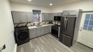 A modern kitchen with grey cabinets, a stainless steel refrigerator, a built-in oven, and a washing machine. - 4 Beds • Parking • Netflix • W/D • Fast Wifi (Wilkes-Barre)