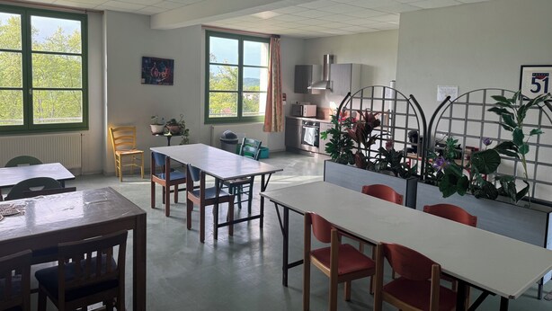 A classroom with tables and chairs, a radiator, a window with a view, and a plant in the corner. - Welcome to Auberge les Clarisses with its relaxation area, communal kitchen (Gourdon)