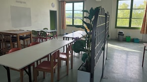 A classroom with tables and chairs, a whiteboard, a clock, and windows with a view of greenery. - Welcome to Auberge les Clarisses with its relaxation area, communal kitchen (Gourdon)