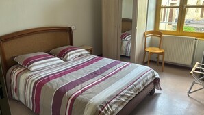 A bed with a striped bedspread, a wooden chair, a radiator, and a window with a view of buildings. - Welcome to Auberge les Clarisses with its relaxation area, communal kitchen (Gourdon)