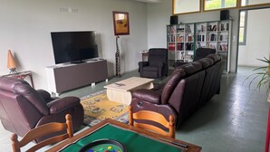 A living room with a billiards table, leather chairs, a television, a bookshelf, and a large window. - Welcome to Auberge les Clarisses with its relaxation area, communal kitchen (Gourdon)