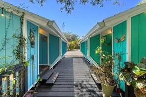 A pathway leading to a row of blue cabins with a wooden deck and potted plants.