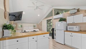 Una cocina moderna con armarios blancos, encimera de madera, ventilador de techo, microondas y refrigerador.