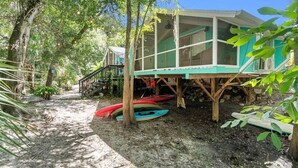 Una estructura de madera con un porche cubierto, kayaks y una escalera que lleva a un edificio verde.