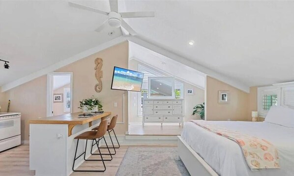 A bedroom with a bed, a desk, a chair, a TV, and a ceiling fan.