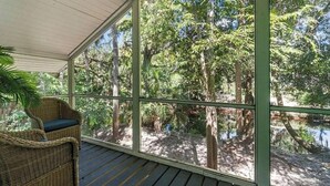 Un espacio al aire libre techado con una silla de mimbre, paredes de vidrio y vistas a una zona boscosa.
