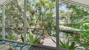 Un invernadero con amplios ventanales de vidrio, una terraza de madera y una gran variedad de plantas tropicales.