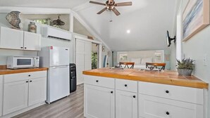 Una cocina con armarios blancos, microondas, ventilador de techo y encimera de madera.