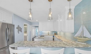 A kitchen with white cabinets, a marble countertop, and pendant lighting. - Beachfront Living | Private Access + Ocean Views (Key Colony Beach)