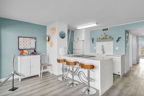 A modern kitchen with a white island, bar stools, a white refrigerator, and a wall-mounted clock. - Oceanview Condo w/ Pool + Direct Beach Access (Marathon)