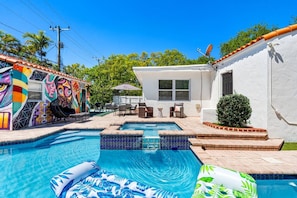 A swimming pool with a tiled edge, surrounded by a patio area with outdoor furniture. - Spanish-Style Modern Home | Heated Pool + Hot Tub (Miami)