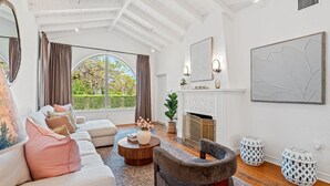 Een ruime woonkamer met een open haard, een groot raam en een moderne kroonluchter.