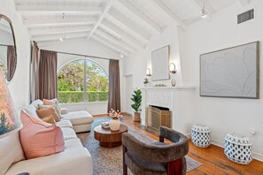 A spacious living room with a fireplace, a large window, and a modern chandelier. - Spanish-Style Modern Home | Heated Pool + Hot Tub (Miami)