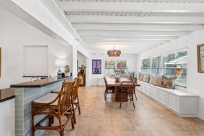 A spacious kitchen with a dining area, white cabinetry, and a large window with blinds. - Spanish-Style Modern Home | Heated Pool + Hot Tub (Miami)