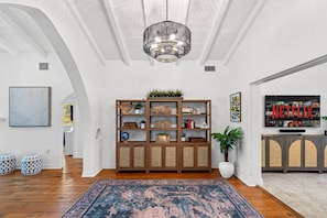 A spacious living room with a wooden bookshelf, a large rug, and a television displaying the Netflix logo. - Spanish-Style Modern Home | Heated Pool + Hot Tub (Miami)