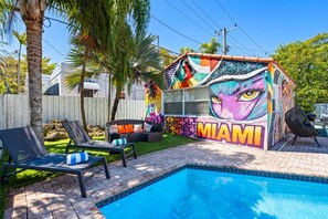 A poolside area with a colorful mural, lounge chairs, and a clear blue pool. - Spanish-Style Modern Home | Heated Pool + Hot Tub (Miami)