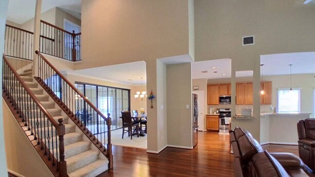 A spacious living area with a wooden staircase, a dining area, and a kitchen. - Lake Houston Retreat | Walk to Lake + Golf | 4BR (Humble)