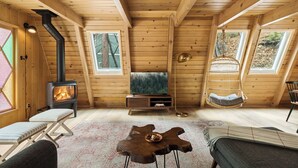 Ein gemütliches Blockhäuschen-Interieur mit Kaminofen, Fernseher, Hängesessel und einem einzigartigen Holztisch.