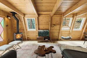 Ein gemütliches Blockhäuschen-Interieur mit Kaminofen, Fernseher, Hängesessel und einem einzigartigen Holztisch.