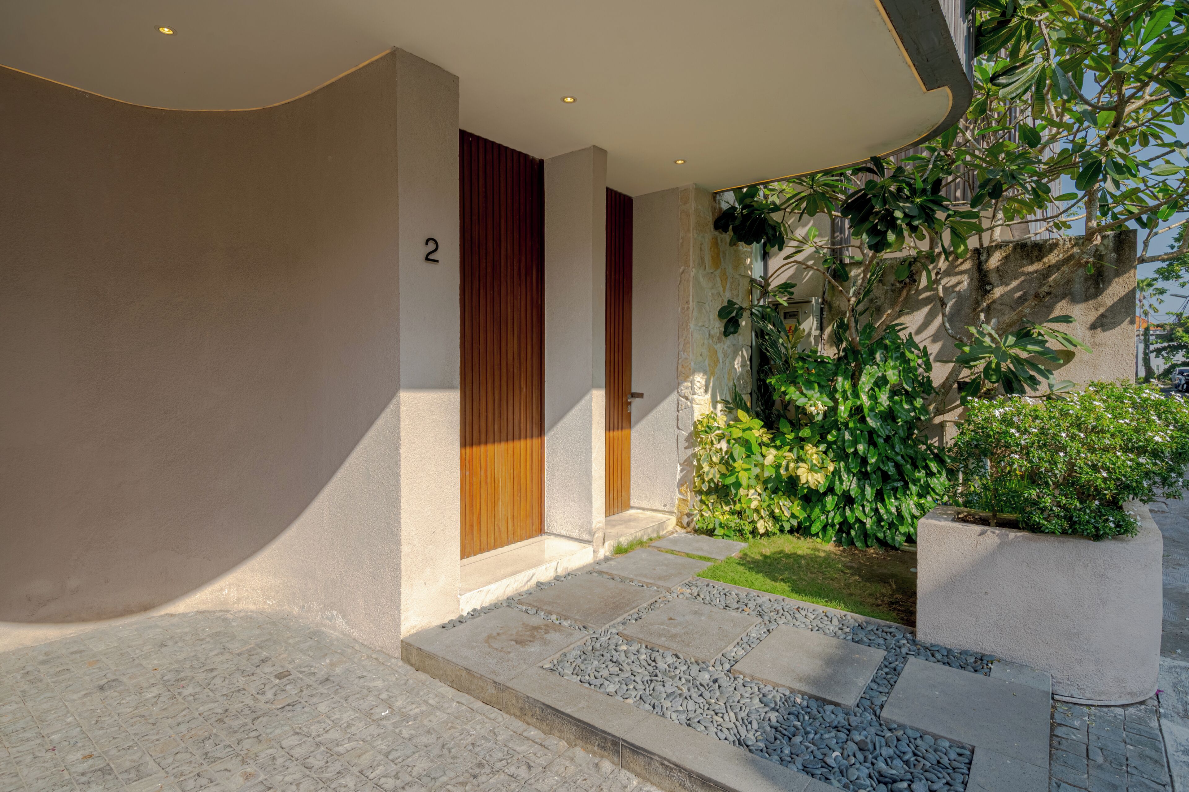 A modern building entrance with a stone pathway, a wooden door, and a number '2' on the wall.