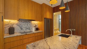 A modern kitchen with wooden cabinets, a marble countertop, a built-in refrigerator, and pendant lighting. - Lumea Canggu by Pertama Stay (Canggu)