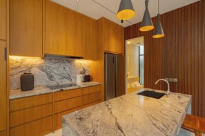 Eine moderne Küche mit Holzschränken, einer Marmorarbeitsplatte, einem integrierten Kühlschrank und Pendelleuchten.