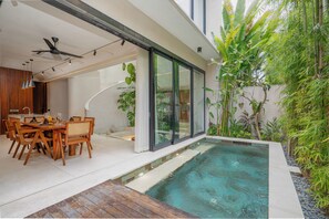 Uma área moderna da piscina com espreguiçadeiras e mesas, rodeada por vegetação exuberante e uma piscina cristalina.