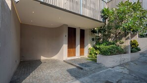 A modern building with a curved facade, a covered entrance, and a small garden area. - Lumea Canggu by Pertama Stay (Canggu)