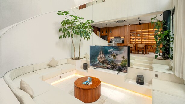 A modern interior with a curved white sofa, a wooden coffee table, and a kitchen area visible through a glass partition. - Lumea Canggu by Pertama Stay (Canggu)