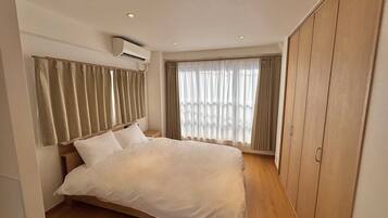 A bedroom with a bed, curtains, an air conditioning unit, and a wardrobe.