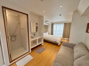 Ein modernes Hotelzimmer mit Dusche, einem Bett, einem Sofa, einem Nachttisch und einem Spiegel.