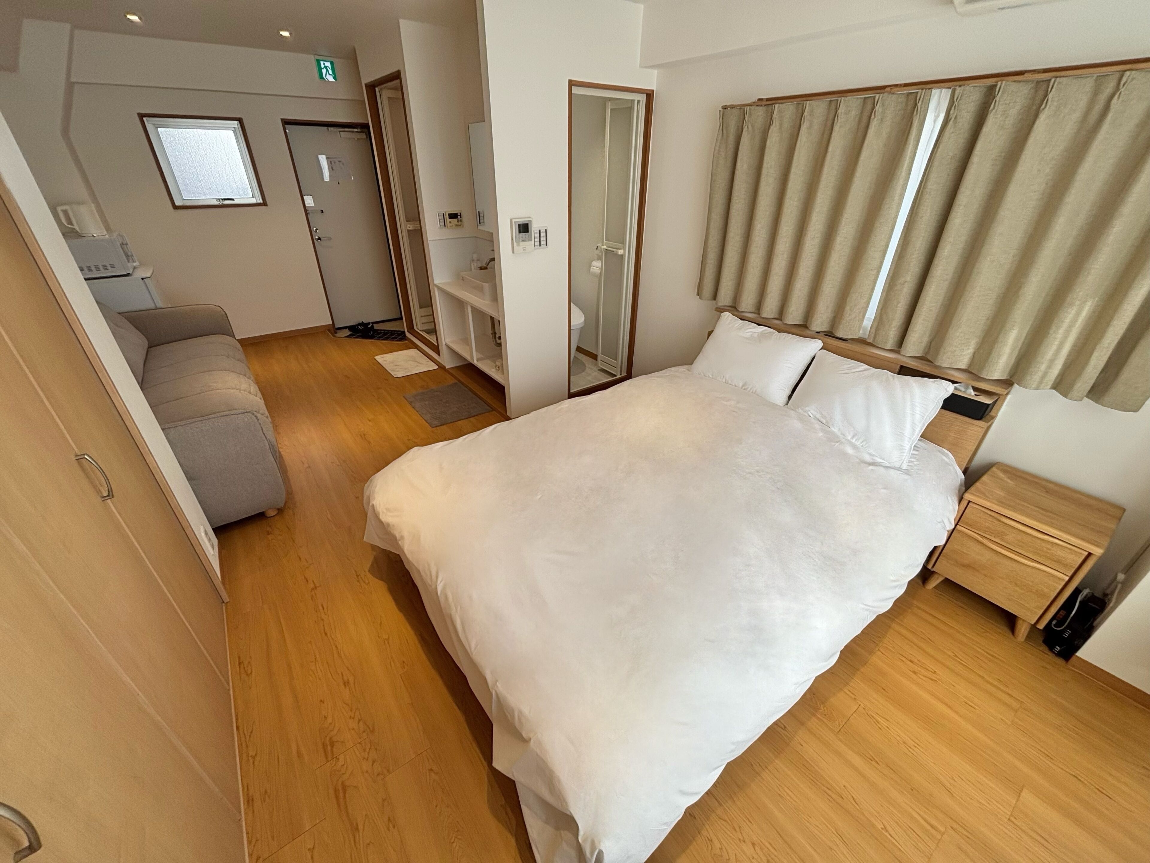 A hotel room with a large bed, bedside tables, a wardrobe, a sofa, and a bathroom with a shower.