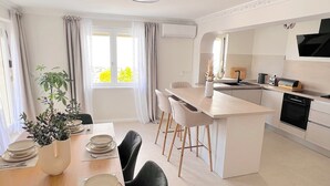 A modern kitchen with a central island, a dining area with a table set for four, and a view of the outdoors through the window. - Luxury Beach Villa, Sibenik, 4 Stars (Brodarica)