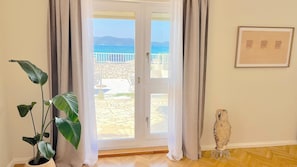 A room with a sliding glass door leading to a patio with a stone floor and a view of the sea.