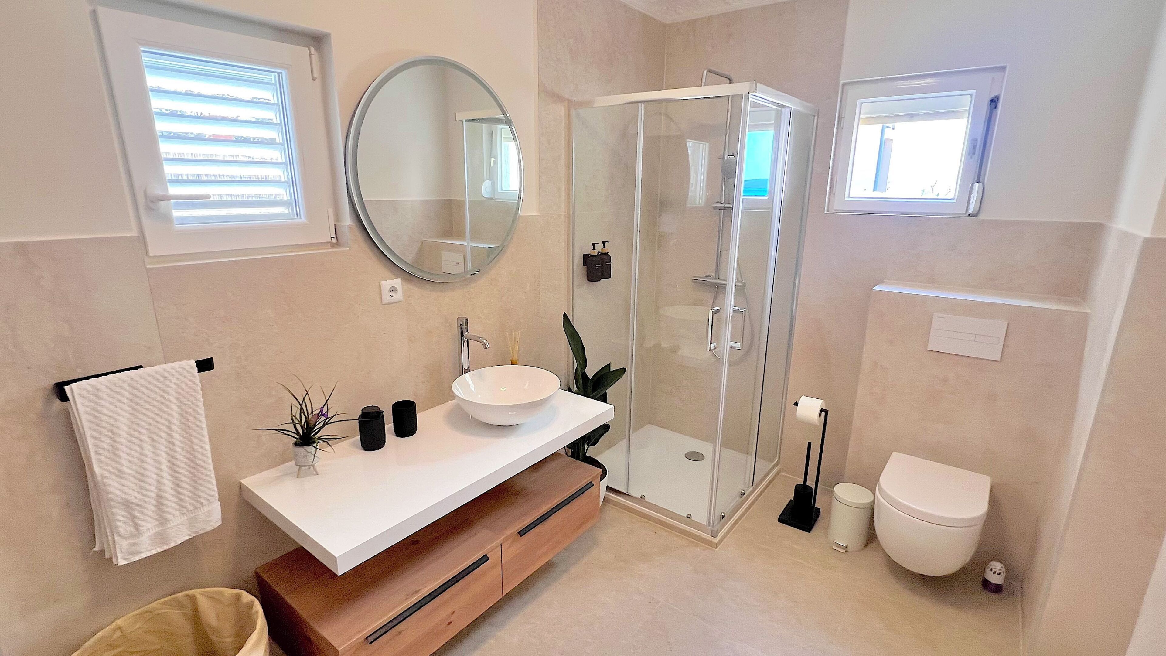 A modern bathroom with a glass shower enclosure, a white sink, and a toilet.