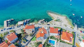 An aerial view of a coastal residential area with houses, a swimming pool, and boats in the water.