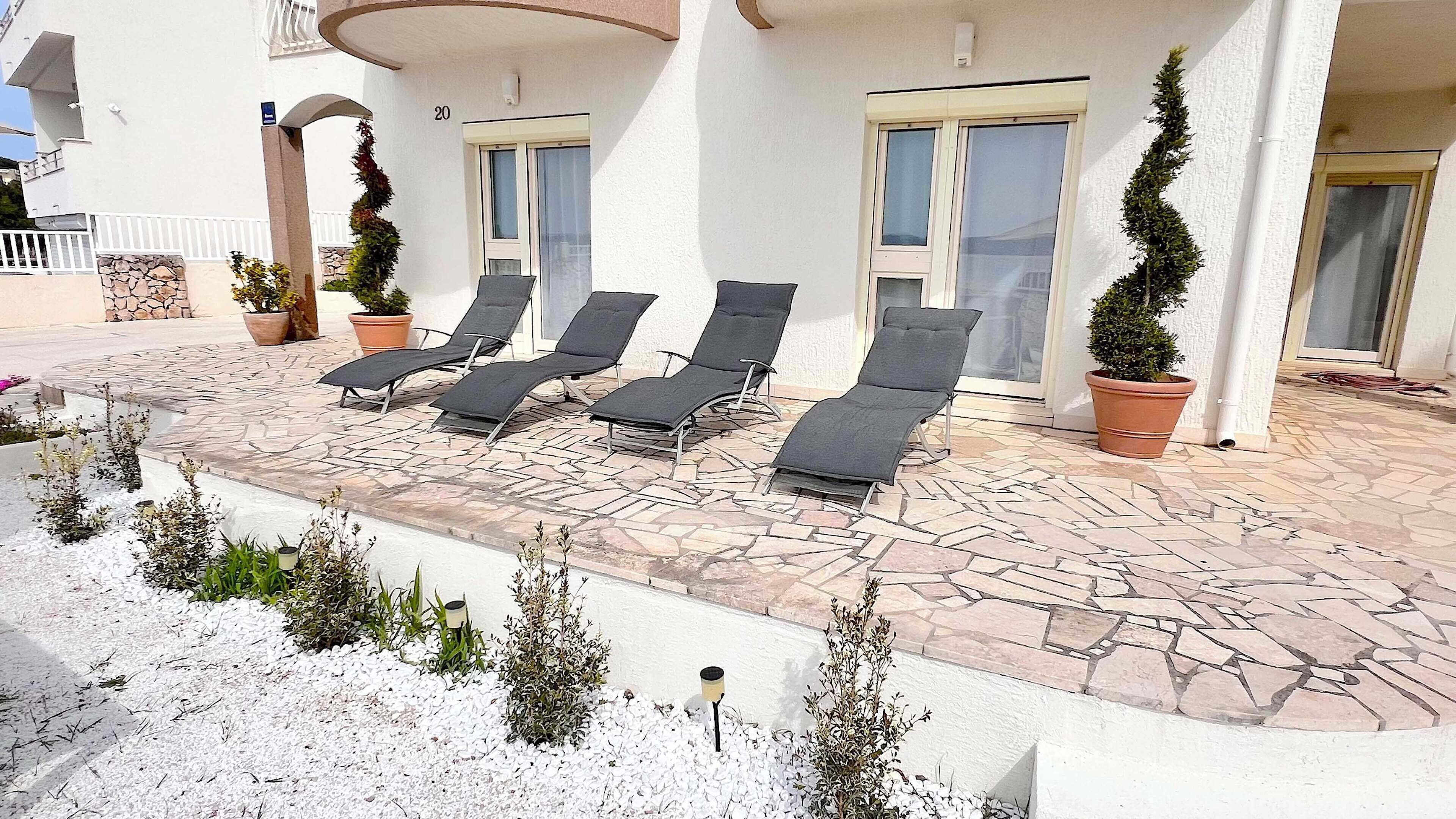 Edificio con patio empedrado de piedra, número 20, con cuatro sillones de descanso y plantas en macetas.