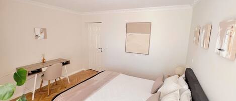 A bedroom with a bed, bedside table, chair, desk, and a mirror on the wall.