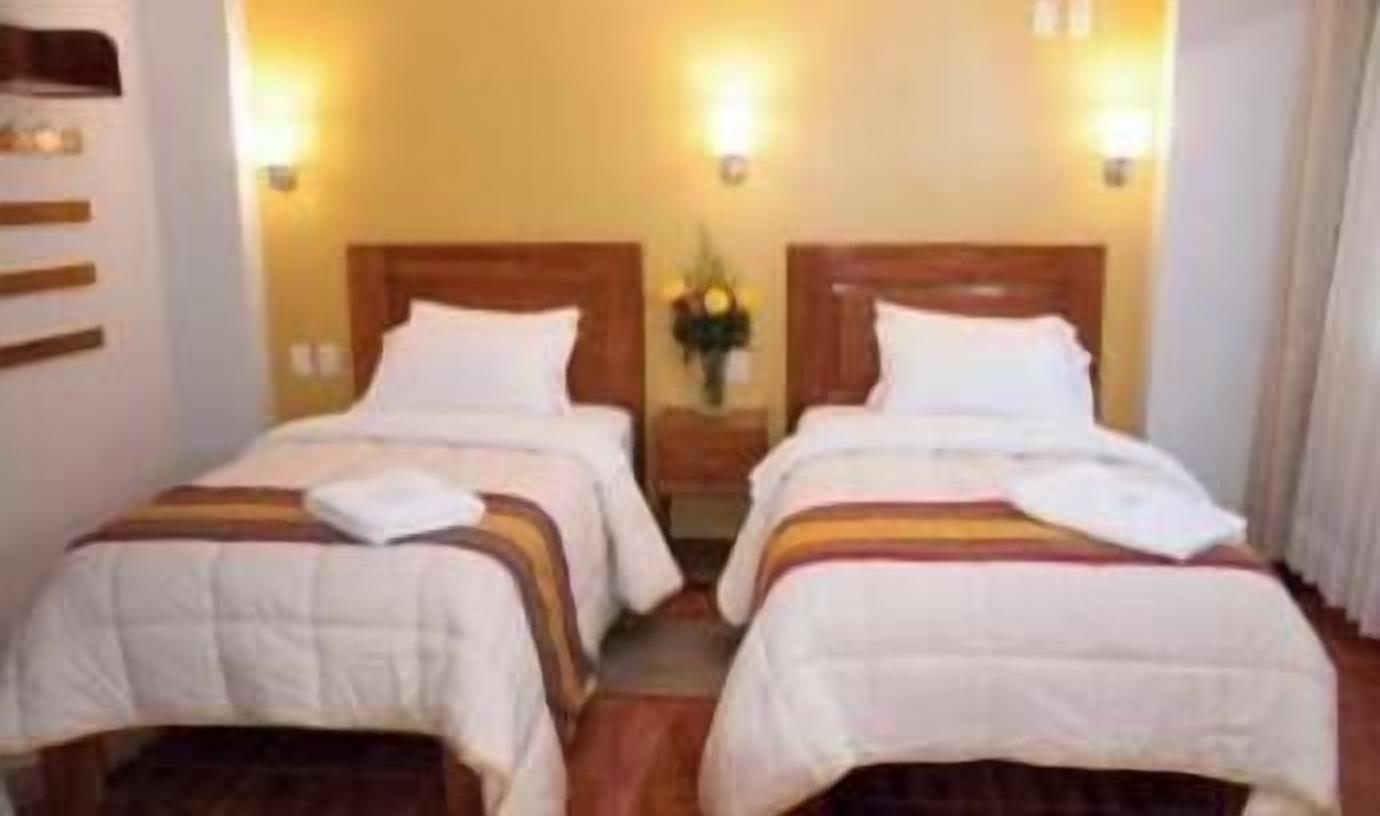 Habitación de hotel con dos camas, cada una con cabecero de madera, ropa de cama blanca y una mesita con un florero entre las camas.