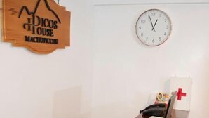 A wooden sign with text, a wall clock, a laptop, and decorative items on a table. - Machu Picchu Picos House (Machu Picchu)