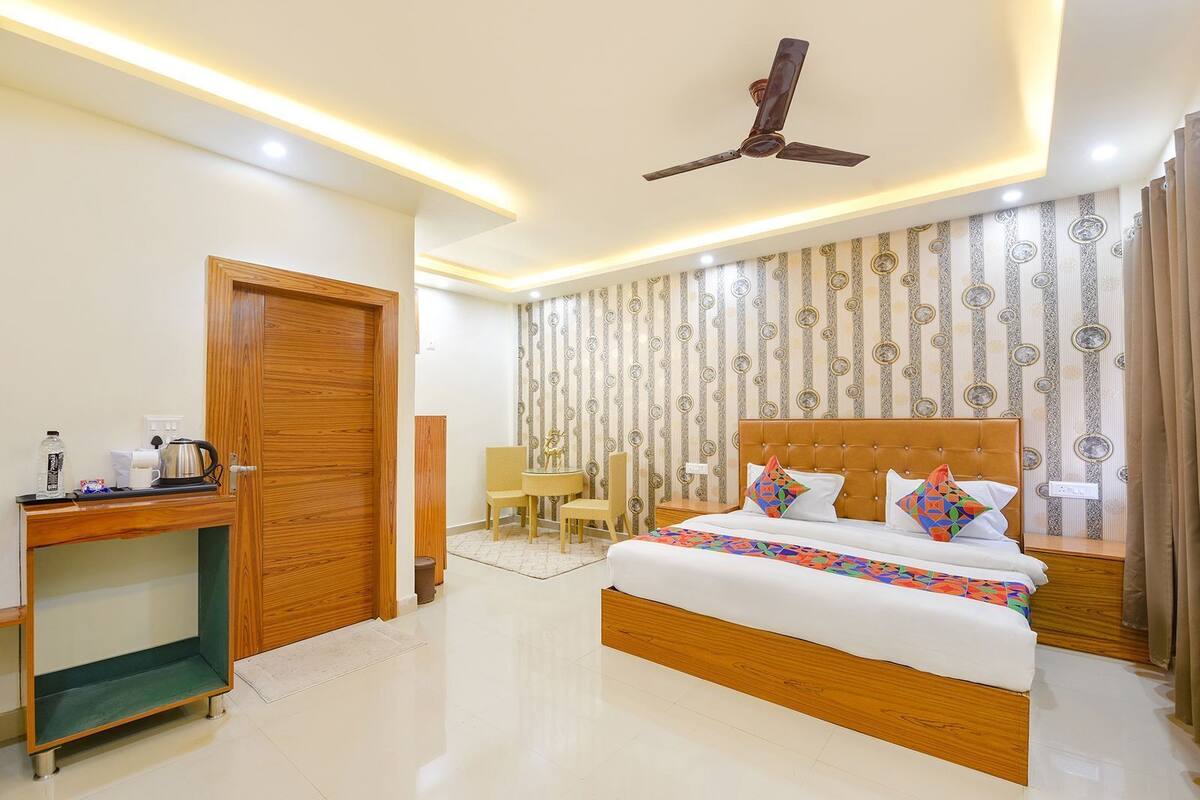 A hotel room with a bed, a desk, a chair, a ceiling fan, and patterned wallpaper.