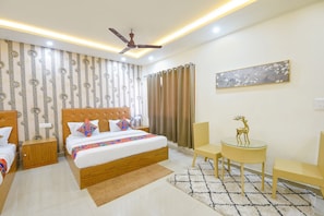 Una habitación de hotel con una cama, dos mesitas de noche, un ventilador de techo, una pequeña mesa con sillas y un cuadro en la pared.