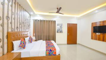 A hotel room with a bed, a wooden headboard, a ceiling fan, a television mounted on the wall, and a door.