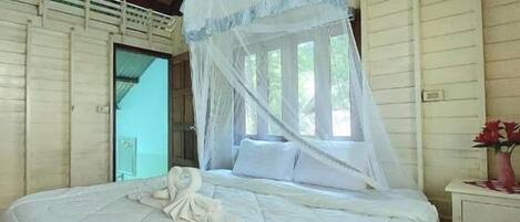 A single bed with a canopy, a bedside table with a vase of flowers, and a window with curtains.