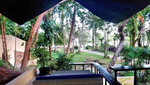 An outdoor seating area with a covered section, surrounded by trees and a pathway.