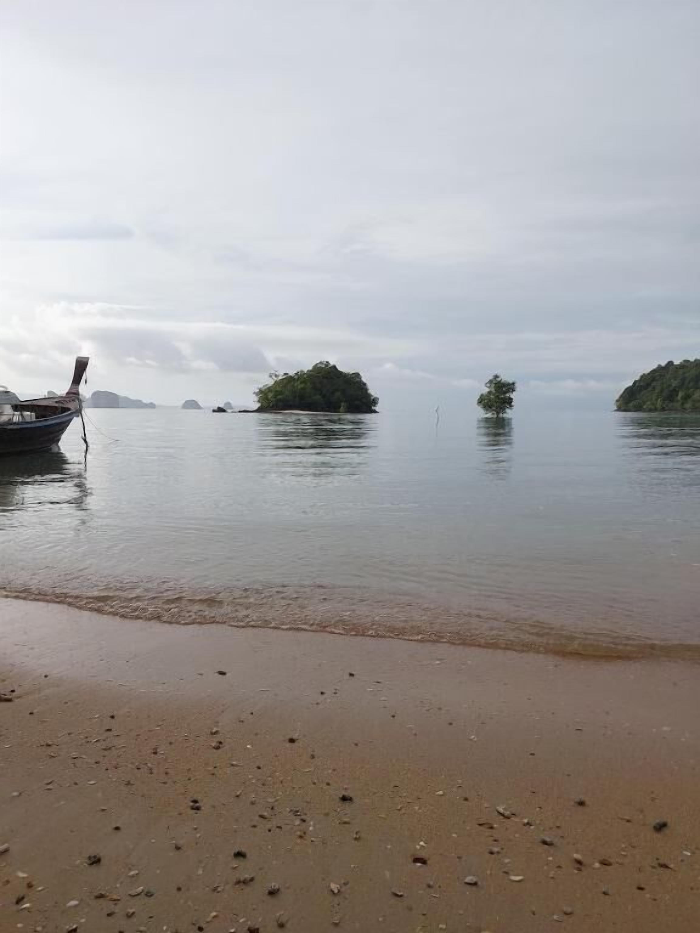 Une plage paisible avec un bateau amarré sur le rivage, une plage de sable et plusieurs petites îles visibles au loin.