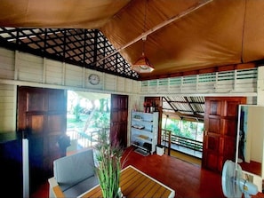 A room with a wooden ceiling, a clock, a fan, and a view of greenery outside. - Wooden House On The Bay (Ko Yao)